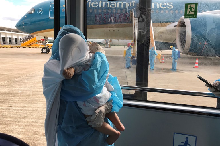 Một phụ nữ Việt Nam mặc đồ bảo hộ bế con về Việt Nam từ chuyến bay giải cứu từ Singapore hôm 7-8-2020. Reuters